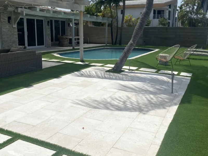 Travertine deck and stepping pads framed in artificial turf by the pool