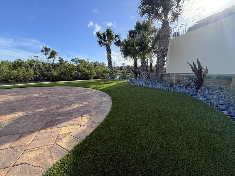 Curved artificial turf edge with paver patio and river rock in Englewood