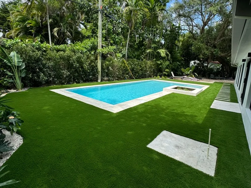 Artificial grass lawn around a pool framed by tropical hedges