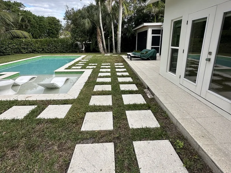 Naples pool yard with patchy, weedy grass between stepping pads before artificial turf