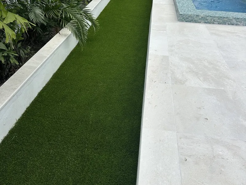 Artificial turf strip between planters and a travertine pool deck in Naples
