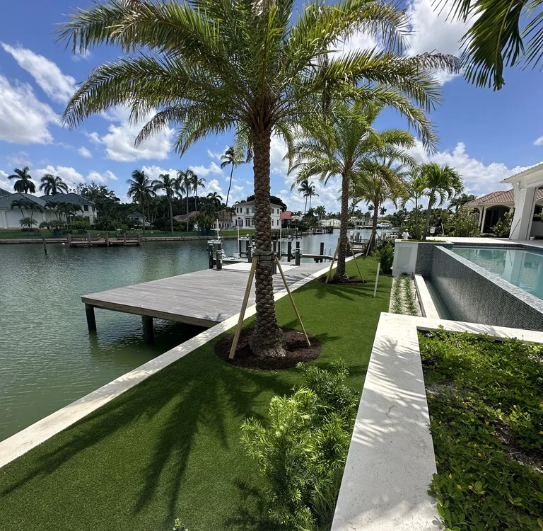 Waterfront artificial grass lawn with palms, dock and pool by Creative Grounds