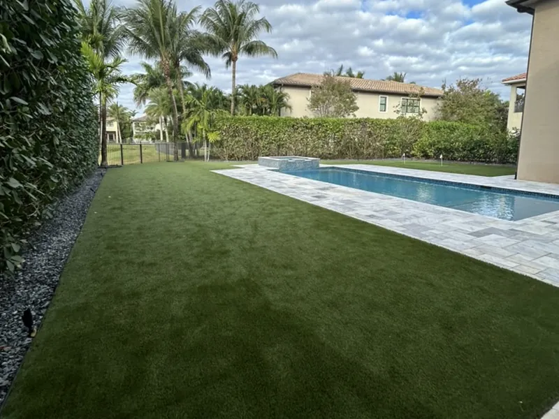 Artificial grass lawn beside a travertine pool with hedge and palms