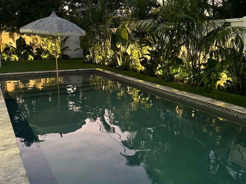 Tropical pool courtyard with accent lighting on palms and plants in the evening