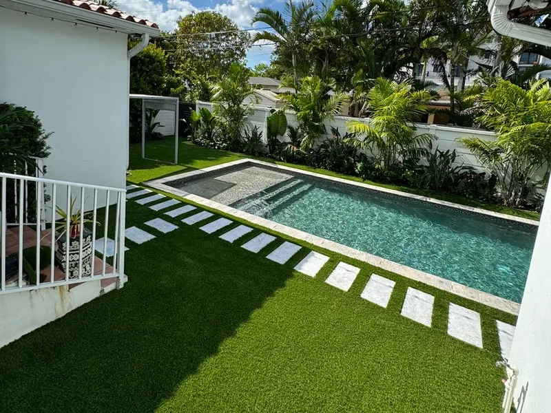 Artificial turf around a pool with a tropical garden
