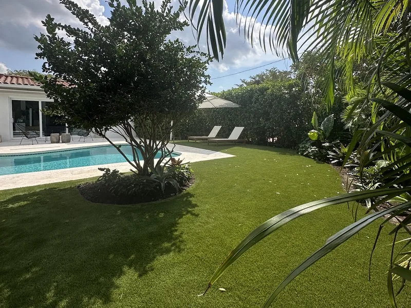 Artificial grass lawn with tree ring beside a pool and tropical garden